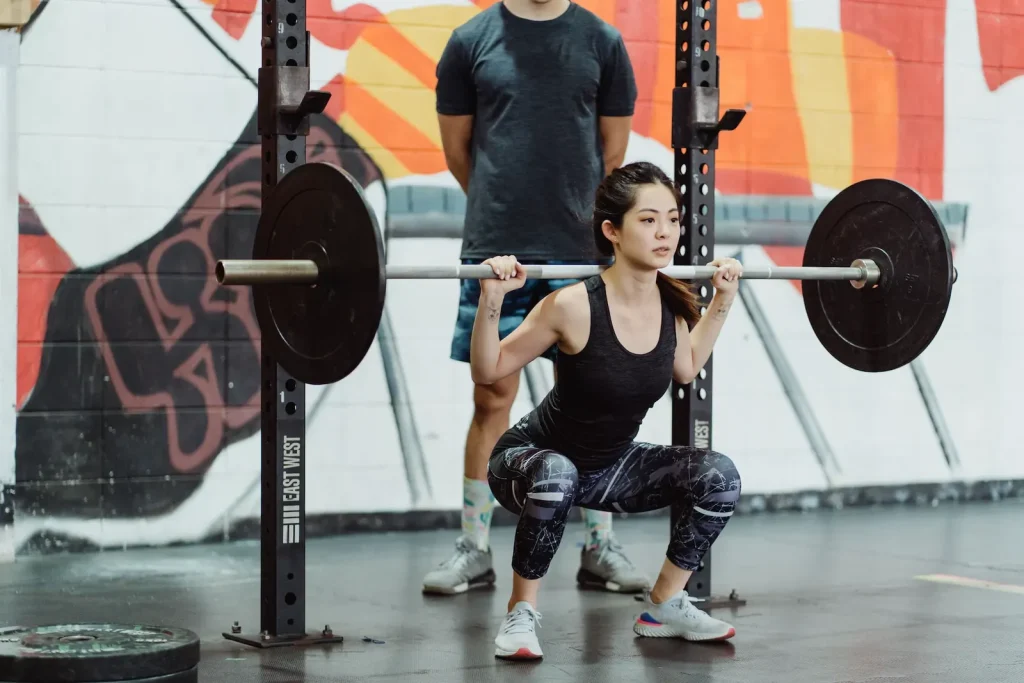 Woman doing a barbell back squat in a gym with a coach watching