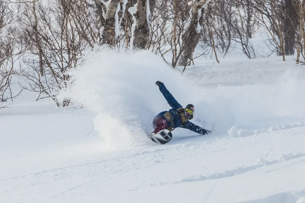 Snowboarder throwing a spray of deep powder while carving through birch trees in Niseko