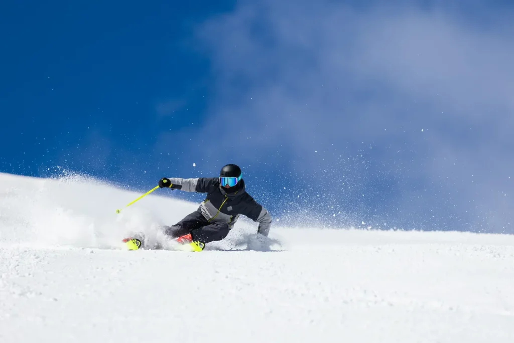 Skier leaning into a fast carved turn on a groomed Niseko slope under a deep blue sky